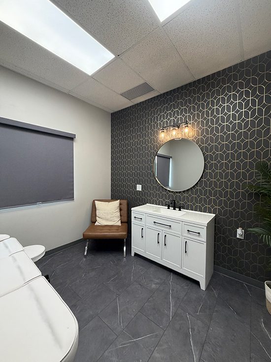 Lashes by Lexi studio vanity with round mirror, glass sconces, and gold geometric wallpaper